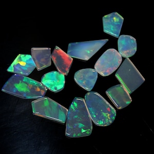 May include: Assortment of iridescent opal gemstones in various shapes and sizes. The opals are a mix of green, blue, red, and white.