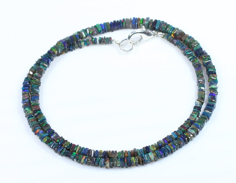 May include: A silver necklace with a silver clasp, featuring a double strand of dark green, blue, and iridescent black square-shaped opal beads.