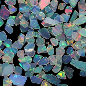 May include: A collection of iridescent opal gemstones in various shapes and sizes. The opals are a mix of white, blue, green, and pink.