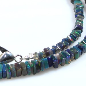 May include: A silver chain necklace with a silver clasp. The necklace is made of dark blue, green, and black iridescent square-shaped beads.