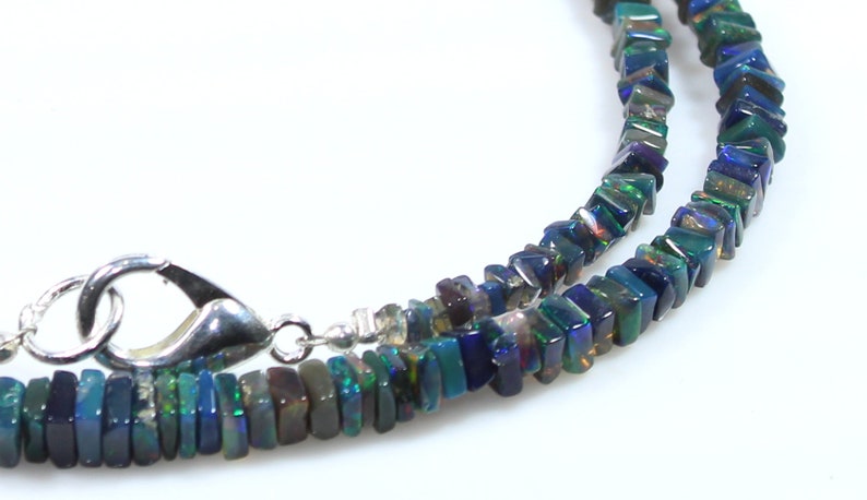 May include: A silver chain necklace with a silver clasp. The necklace is made of dark blue, green, and black iridescent square-shaped beads.