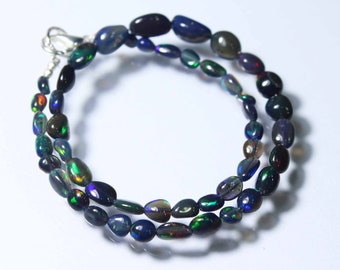 May include: A strand of black opal beads with iridescent flashes of color. The beads are oval shaped and strung on a silver chain.