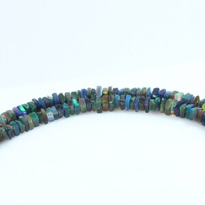 May include: A strand of dark green, blue, and black opal beads. The beads are rectangular and have a slightly irregular shape. The beads are strung on a clear thread.