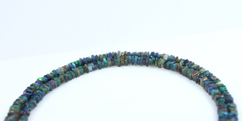 May include: A strand of dark green, blue, and black opal beads. The beads are rectangular and have a slightly irregular shape. The beads are strung on a clear thread.