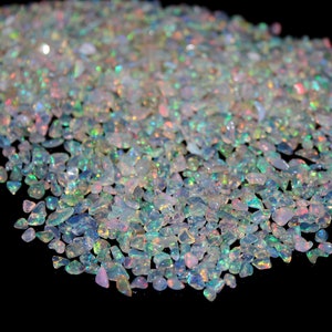 May include: A pile of iridescent opal chips in various sizes and shapes. The chips are a mix of white, blue, green, and pink.