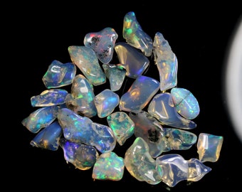 Puede incluir: Una colección de piedras preciosas de ópalo iridiscente en varias formas y tamaños. Los ópalos son una mezcla de azul, verde y blanco.