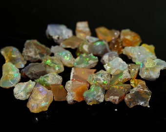Puede incluir: Una colección de piedras preciosas de ópalo en bruto y sin pulir con formas y texturas irregulares. Las piedras muestran una variedad de colores que incluyen blanco translúcido, marrón terroso y destellos vibrantes de verde, naranja y azul.