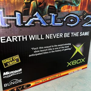 May include: A video game poster for Halo 2, featuring a green and black Xbox logo, the text "Earth will never be the same", and the text "Only on Xbox".