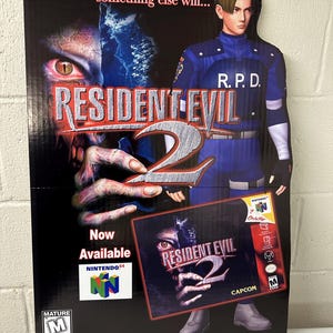 May include: A cardboard stand-up cutout advertisement for the video game Resident Evil 2 for the Nintendo 64. The cutout features a character from the game wearing a blue uniform with the letters R.P.D. on the chest. The character is holding a game cartridge for Resident Evil 2. The text "If the suspense doesn't kill you, something else will..." is at the top of the cutout. The text "Now Available" is at the bottom of the cutout.