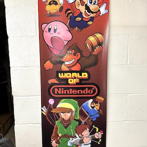 Może przedstawiać: Pionowy baner przedstawiający postacie z serii gier wideo World of Nintendo. Baner jest czerwony, brązowy i czarny z białym logo Nintendo. Postacie to Mario, Donkey Kong, Link i Kirby.