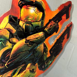 May include: A green and yellow action figure of a soldier wearing a helmet and holding a gun. The figure is standing on a red and orange background.
