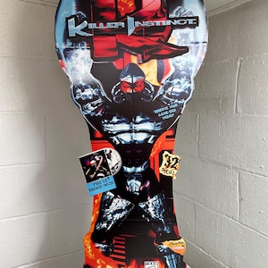 Op de afbeelding: Een hoge, verticale Killer Instinct Super Nintendo promotionele display. Het ontwerp toont een gespierd personage met een rood-zwart kleurenschema, het logo van de game en de tekst "COMING SOON!" en "RESERVE YOUR GAME-PAK TODAY!".
