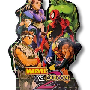 May include: A cardboard cutout featuring characters from Marvel vs. Capcom 2: New Age of Heroes. The artwork includes characters like Ryu, Chun-Li, Spider-Man, Wolverine, and Hulk. The game's logo and the Capcom and Naomi logos are also visible.