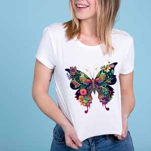 Op de afbeelding: Wit T-shirt met een kleurrijke vlinderprint. De vlinder is gemaakt van bloemen en bladeren in tinten groen, blauw, roze en paars.