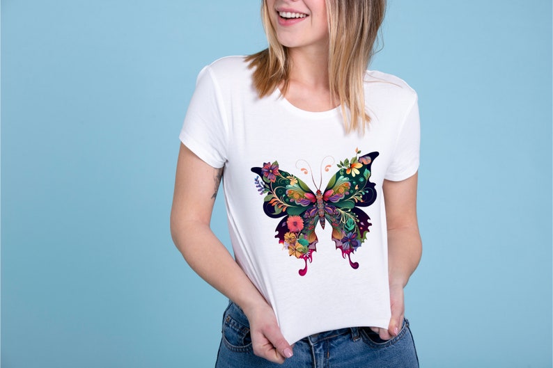 Op de afbeelding: Wit T-shirt met een kleurrijke vlinderprint. De vlinder is gemaakt van bloemen en bladeren in tinten groen, blauw, roze en paars.