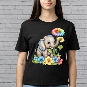May include: A black t-shirt with a colorful illustration of a cartoon elephant with rainbow-colored ears and a rainbow flower. The elephant is surrounded by blue, yellow, pink, and green flowers.