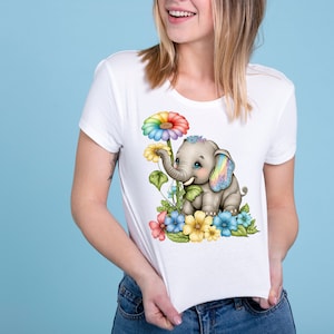 May include: A white t-shirt with a colorful graphic of an elephant with rainbow ears and a rainbow daisy. The elephant is surrounded by colorful flowers.
