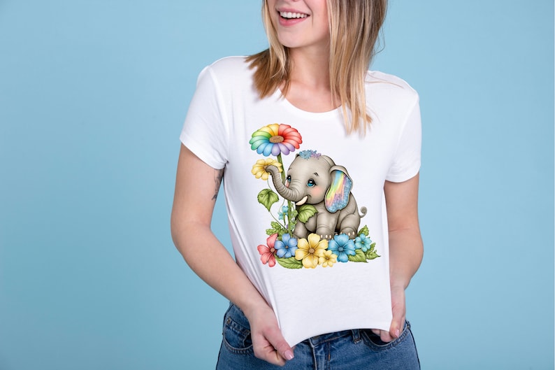 May include: A white t-shirt with a colorful graphic of an elephant with rainbow ears and a rainbow daisy. The elephant is surrounded by colorful flowers.