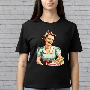 May include: A black t-shirt with a vintage illustration of a woman in a blue and white polka dot dress holding a bowl of popcorn and a cup. The woman is smiling and has a red bow in her hair.