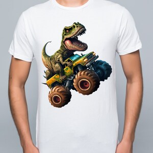 May include: White t-shirt with a green dinosaur riding a yellow monster truck with large tires.