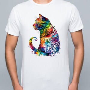 May include: A white t-shirt with a colorful graphic of a cat sitting with its tail curled around its body. The cat is made up of a variety of colors, including blue, green, yellow, orange, and red. The graphic is surrounded by a watercolor effect.
