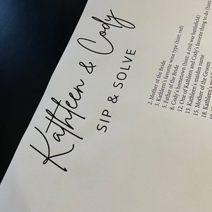 May include: A white card with black text that reads "Kathleen & Cody" and "Sip & Solve". The card lists a series of questions, including "Mother of the Bride", "Kathleen's favorite wine type (hint: red)", and "Cody's hometown (hint: a civil war battlefield)".