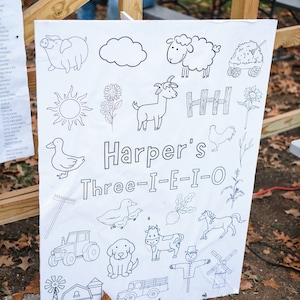 May include: A white sign with black line drawings of farm animals, a tractor, a windmill, a barn, a scarecrow, a sun, a cloud, a fence, a rake, a wagon, and a flower. The sign says "Harper's Three-I-E-I-O".