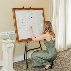 May include: A woman in a green dress is filling out a cocktail crossword puzzle on an easel. The crossword puzzle is titled "Cocktail Crossword Puzzle".