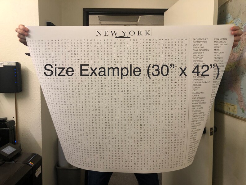 May include: A black and white word search puzzle poster featuring the word "NEW YORK" at the top. The poster is being held by a person's hands and shows a size example of 30 inches by 42 inches. The poster includes a list of words related to New York City.