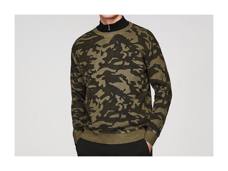 May include: A green and black camouflage print sweatshirt with a round neckline and long sleeves.