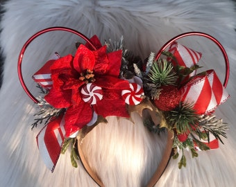 Puede incluir: Orejas de Minnie Mouse de Navidad de temática roja y blanca con una flor de pascua, bastones de caramelo y ramas de abeto.