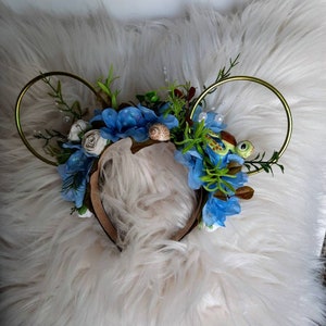 May include: A pair of gold hoop headbands with blue and white flowers, green leaves, a seashell, and a small green turtle charm.