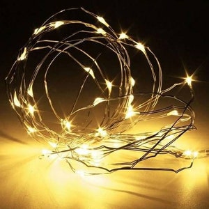 May include: A string of warm white LED fairy lights wrapped in a tangled, decorative pattern. The lights are on a thin, silver wire.