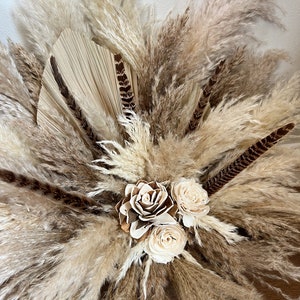 May include: A dried floral arrangement featuring pampas grass, dried palm leaves, and white dried roses. The arrangement is in a natural, earthy color palette.