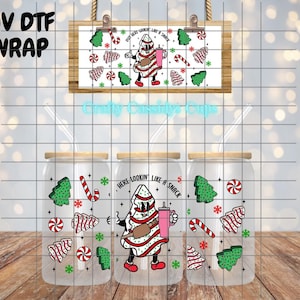 May include: Three glass tumblers with bamboo lids and straws, featuring a Christmas-themed design. The design includes a cartoon Christmas tree character holding a pink drink, candy canes, and Christmas trees. The text "HERE LOOKIN' LIKE A SNACK" is also present.