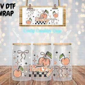 May include: Three glass can-shaped cups with bamboo lids and clear straws. Each cup features a peach design with the words "Just Peachy" and a bow. The design includes a peach, bow, and stars. The words "UV DTF WRAP" are in the upper left.