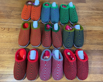 May include: A collection of 12 pairs of knitted slippers in various colors and patterns, including red, green, blue, and brown. Each pair has a size tag attached.