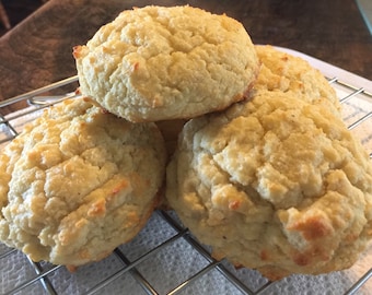 May include: Four golden brown biscuits stacked on a wire rack. The biscuits have a slightly rough texture and are slightly puffy.