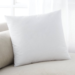 May include: A white pillow with a smooth, soft surface. The pillow is lying on a light brown couch.