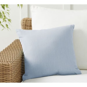 May include: A light blue throw pillow with a soft, textured fabric. The pillow is sitting on a wicker chair with a white cushion.