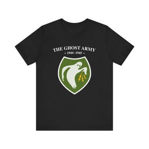 May include: Black t-shirt with a white graphic of a ghost holding lightning bolts. The graphic is inside a green shield with the text "THE GHOST ARMY • 1944-1945 •" above it.