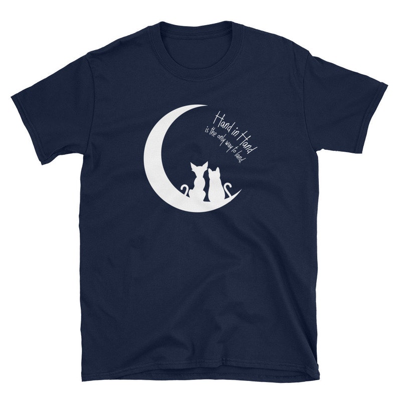 May include: Navy blue t-shirt with a white crescent moon and two cats sitting back to back. The text "Hand in Hand is the only way to lead" is printed on the shirt.