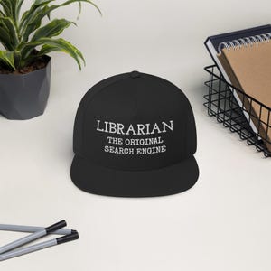May include: Black and white embroidered baseball cap with the text "LIBRARIAN THE ORIGINAL SEARCH ENGINE".