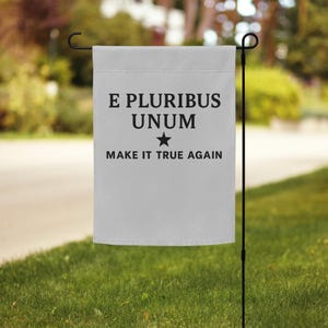 May include: A rectangular white garden flag hanging from a black metal stand. The flag features black text that reads E PLURIBUS UNUM, followed by a small black star, and the text MAKE IT TRUE AGAIN printed in a bold, sans-serif font.