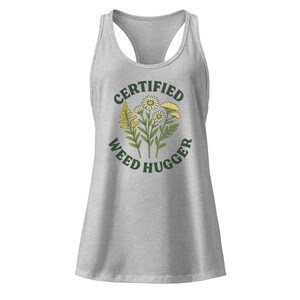May include: A light gray tank top with a racerback design. The front features a circular graphic with the words "CERTIFIED WEED HUGGER" encircling a floral illustration of daisies and other wildflowers in green and yellow.