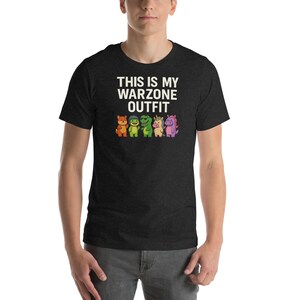 May include: Dark gray t-shirt with the text "THIS IS MY WARZONE OUTFIT" in white. Below the text are cartoon animal characters in various colors. The shirt is short-sleeved and worn by a person.