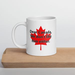 May include: White ceramic coffee mug with a red maple leaf and the text "Dear Canada, We don't like him either."