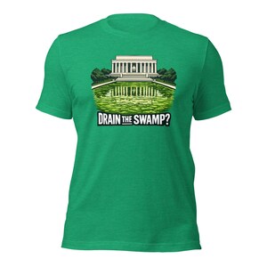 May include: A bright green short-sleeve t-shirt featuring a graphic illustration of the Lincoln Memorial reflected in a green swampy pool. Below the illustration, the text DRAIN THE SWAMP? is printed in bold white capital letters with a black outline.