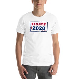Puede incluir: Camiseta blanca con un gráfico rectangular. El gráfico presenta la palabra "TRUMP" en rojo, los números "2028" en azul y las palabras "per gallon" en una fuente más pequeña. El diseño está enmarcado en un borde azul.