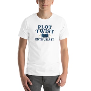 May include: White t-shirt with a blue graphic that says "Plot Twist Enthusiast" with a book icon and a sunburst design.